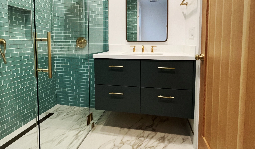 Modern bathroom with a glass-enclosed shower featuring teal subway tiles, a floating vanity with dark drawers and gold hardware, and a marble floor.