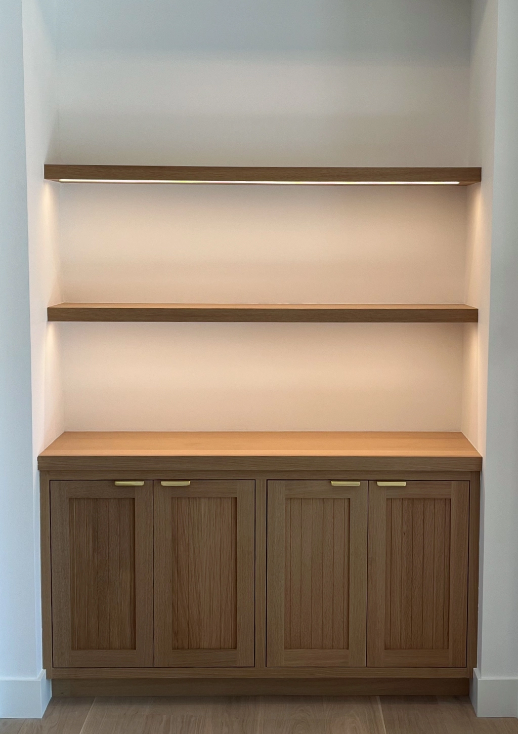 A wooden built-in cabinet with three closed doors and two open shelves above, set within a recessed wall.