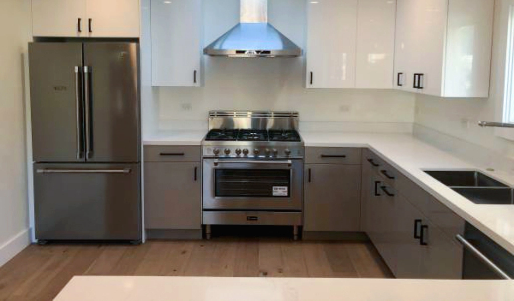 Modern kitchen with stainless steel appliances, including a refrigerator, gas stove with oven, and vent hood. White cabinets and countertops, with a sink on the right side.