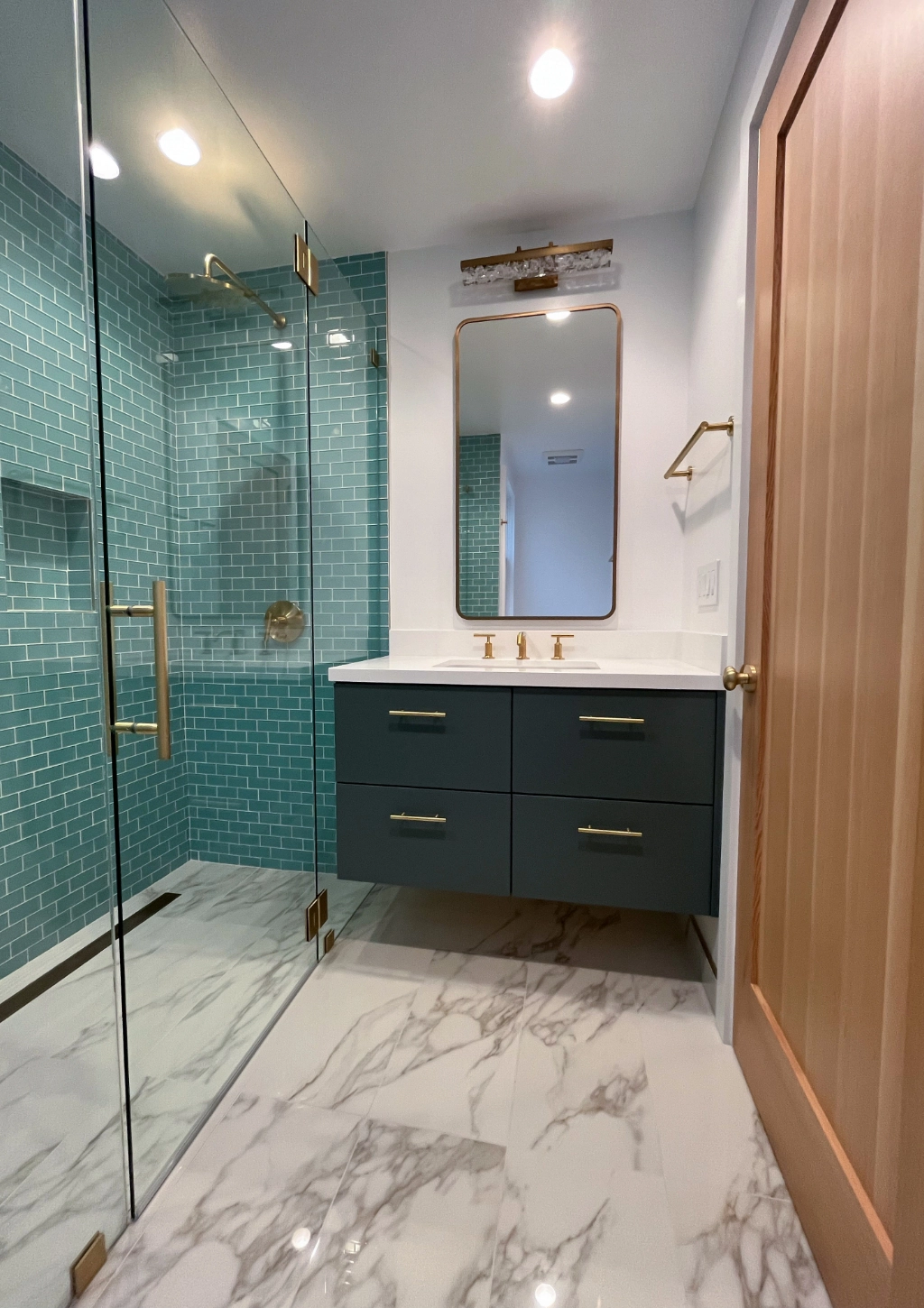 A modern bathroom remodel with blue shower tiles and white marble floor.